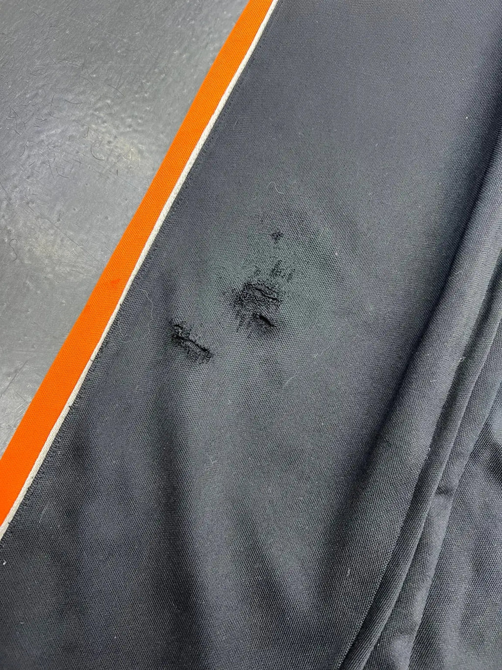 Jaguares track pants — frayed holes and abrasion beside the orange side stripe